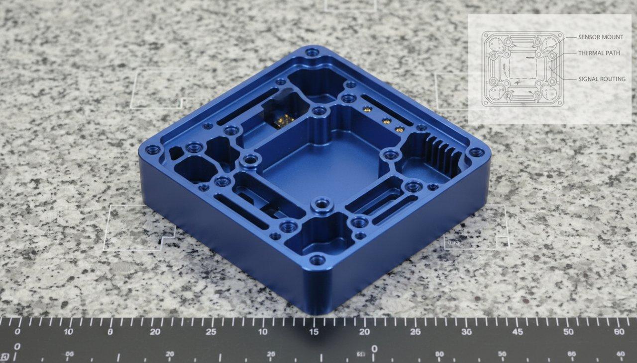 Une enceinte en aluminium anodisé de haute précision et sur mesure pour un capteur robotique, photographiée professionnellement sur une table de mesure. L'image met en évidence sa finition anodisée sombre et lisse ainsi que ses caractéristiques internes complexes, avec un diagramme discret montrant la conception de la cavité interne.